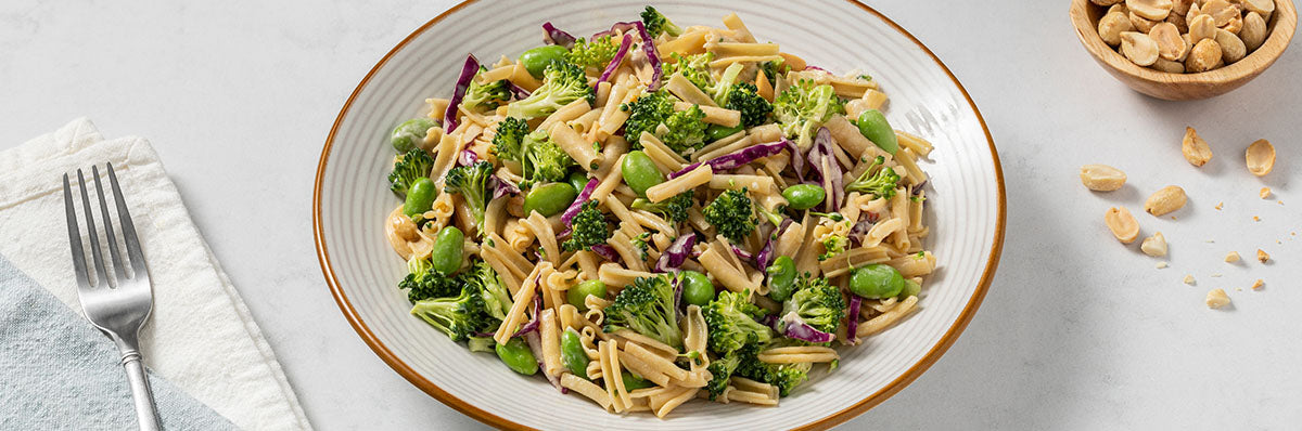 A white bowl full of Pasta Agile, broccoli, and edamame garnished with peanuts