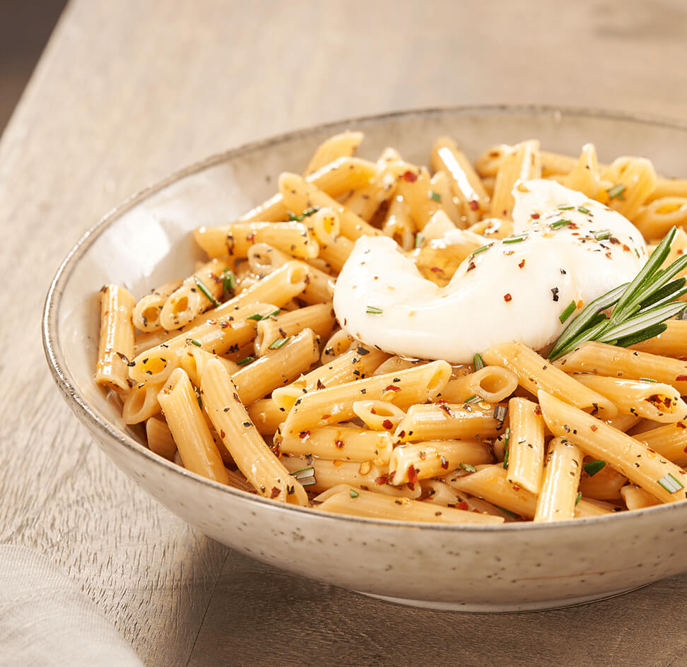 A close up of a bowl of ZENB Penne Pasta garnished with red pepper flakes, rosemary, and burrata cheese.